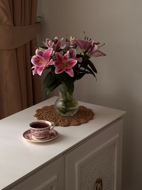 A stylish scene with pink lilies in a vase and a teacup on a decorative table.
