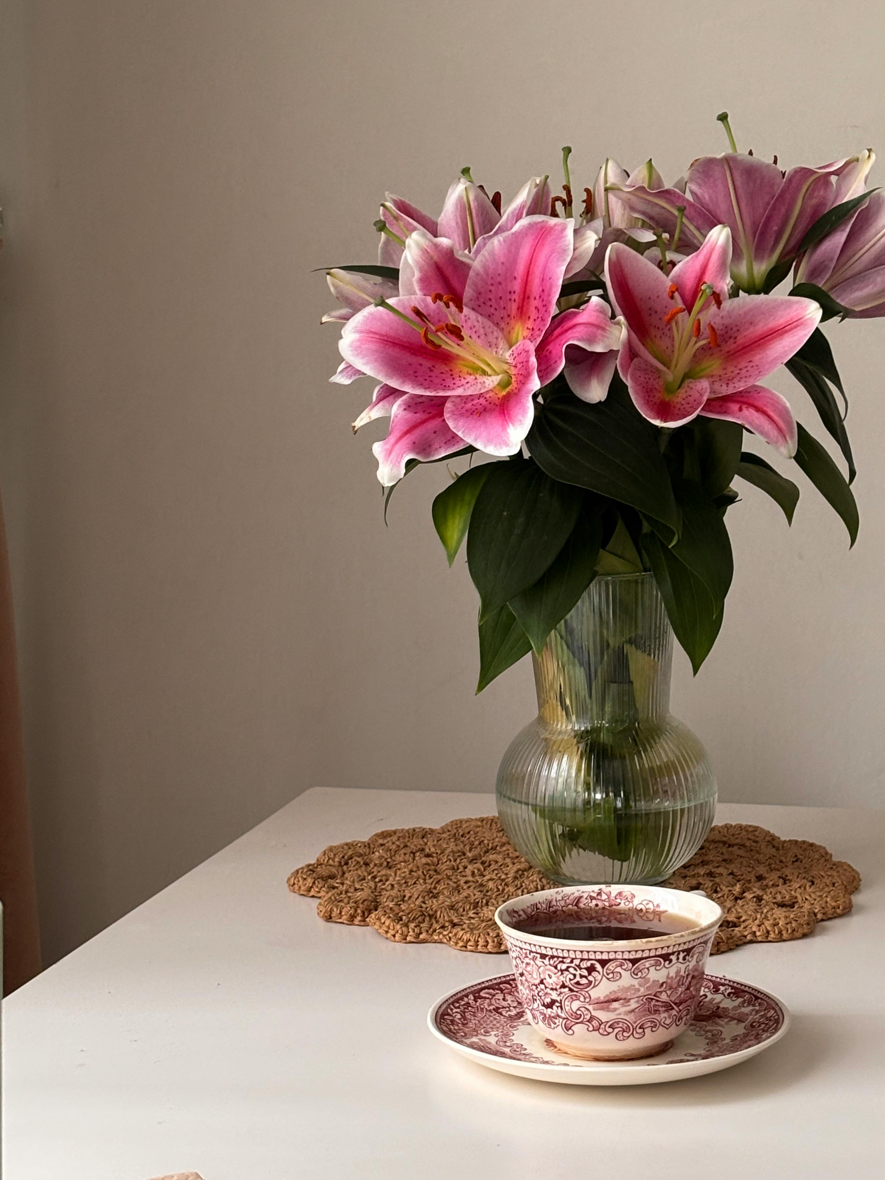 gratis Een levendig boeket lelies in een vaas naast een vintage theekopje op tafel. Stockfoto