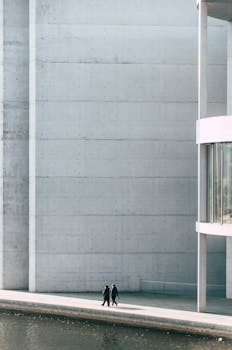 Minimalist view of modern architecture with two people walking along a canal.