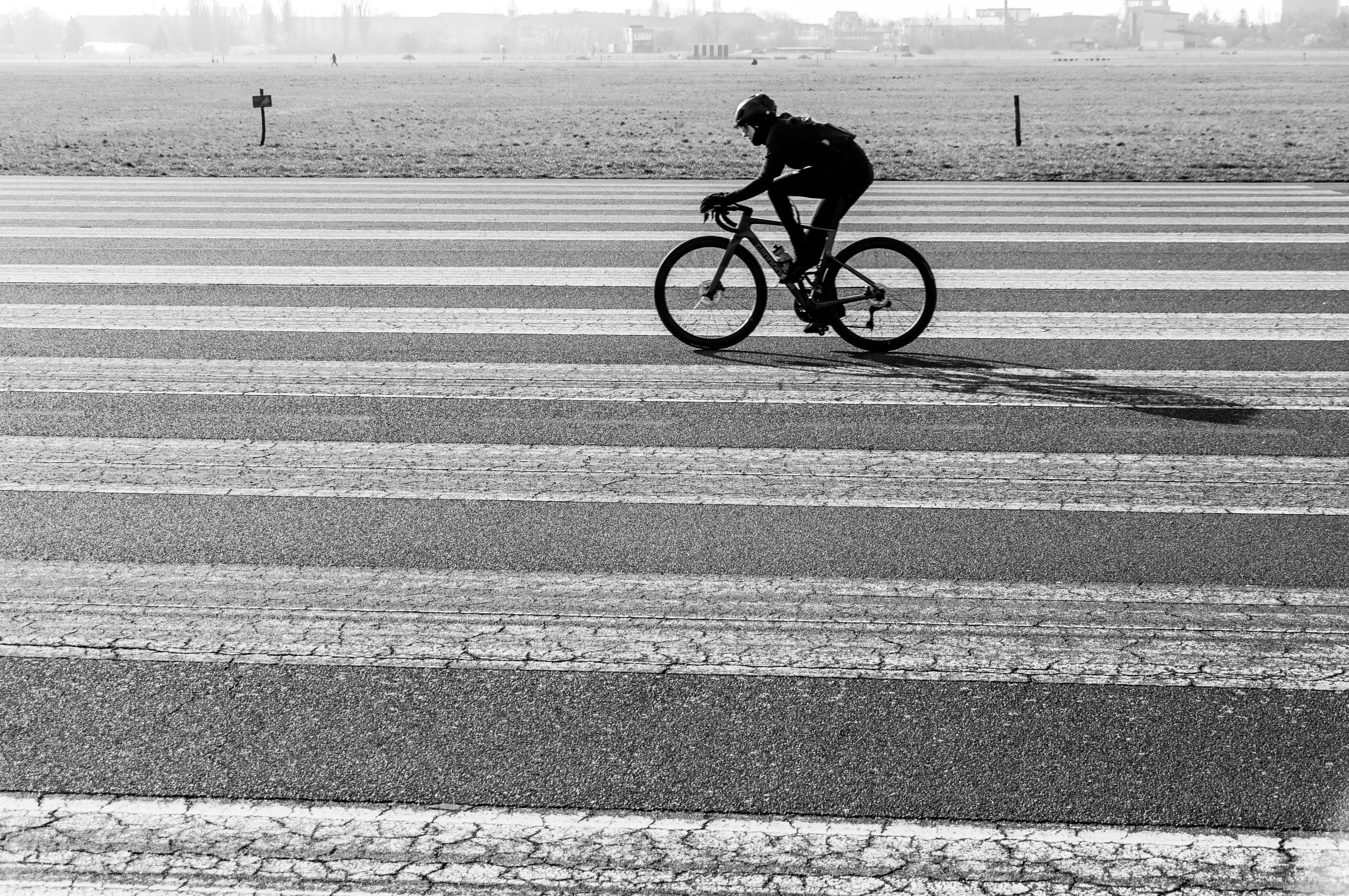 Silhouette of a cyclist riding on a runway with distinct lines, captured outdoors in black and white.