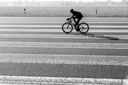 Silhouette of a cyclist riding on a runway with distinct lines, captured outdoors in black and white.