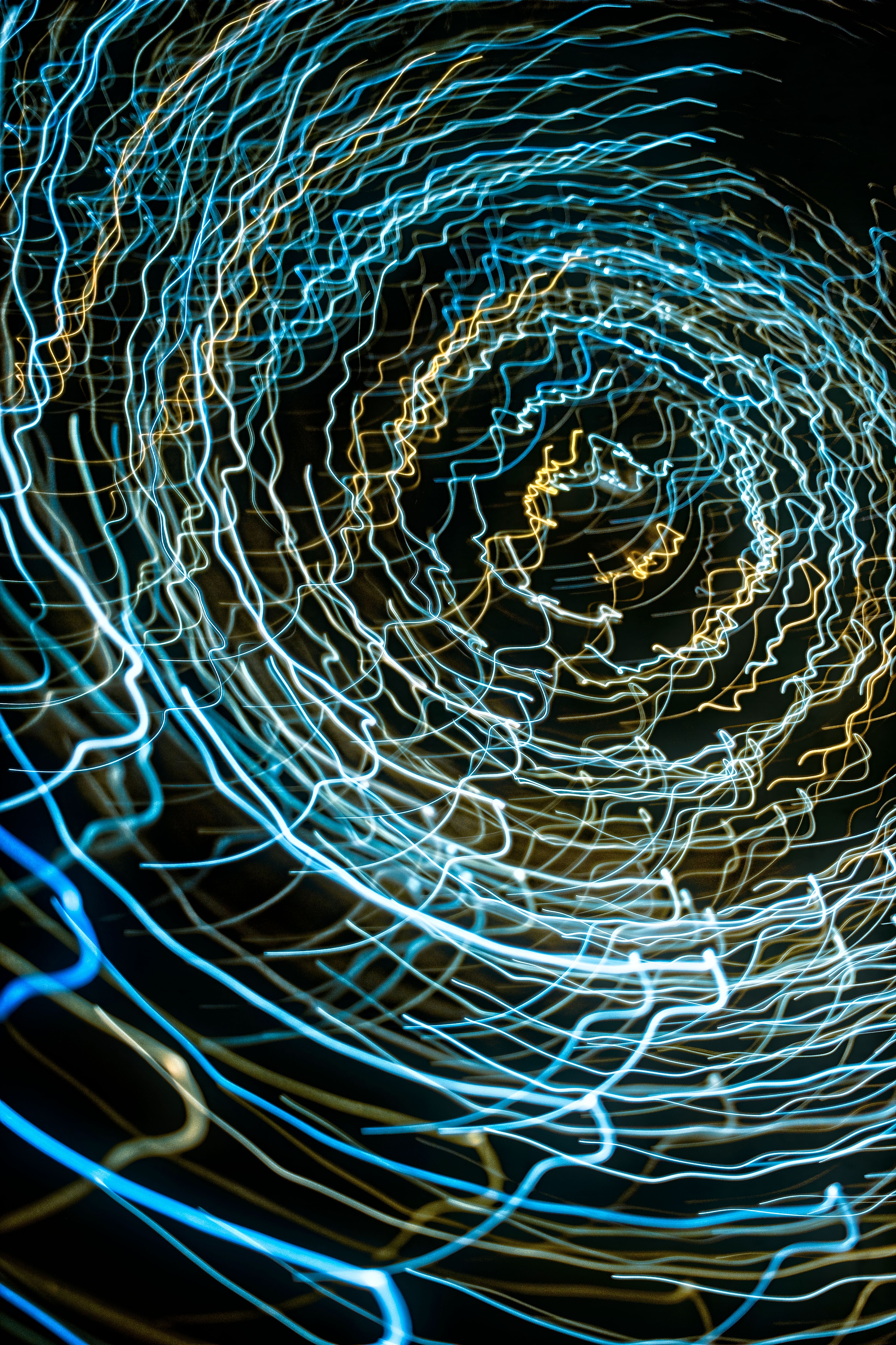 Abstract image of swirling blue and gold light trails creating a dynamic spiral pattern against a dark background.