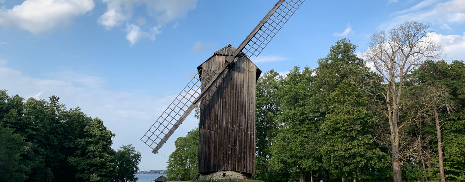 A historic wooden windmill stands amidst lush greenery under a blue sky in Estonia.