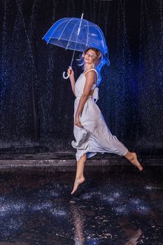 A joyful woman leaps with a clear umbrella under artificial rain at night.