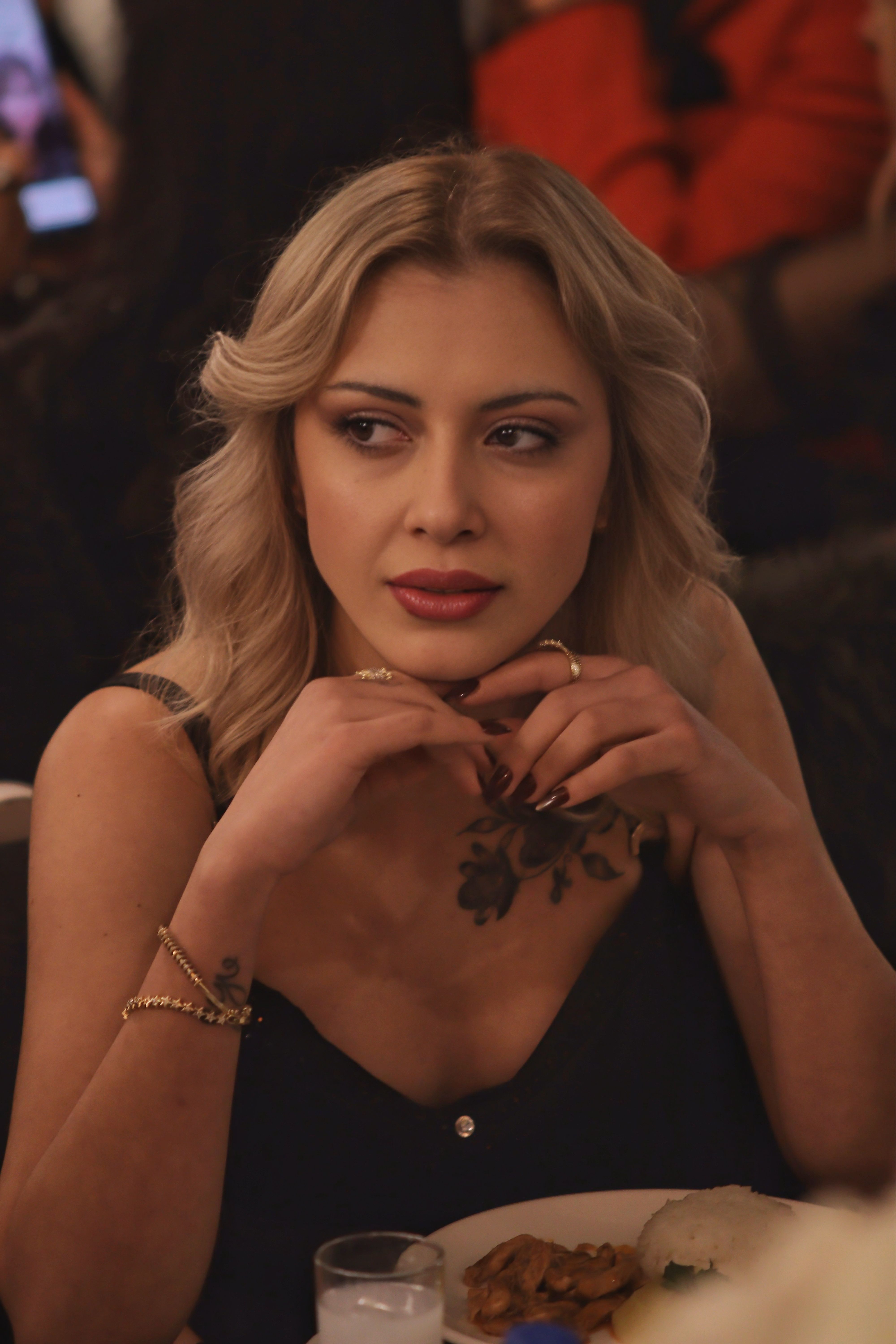 A thoughtful woman with elegant attire enjoying an evening dining experience.