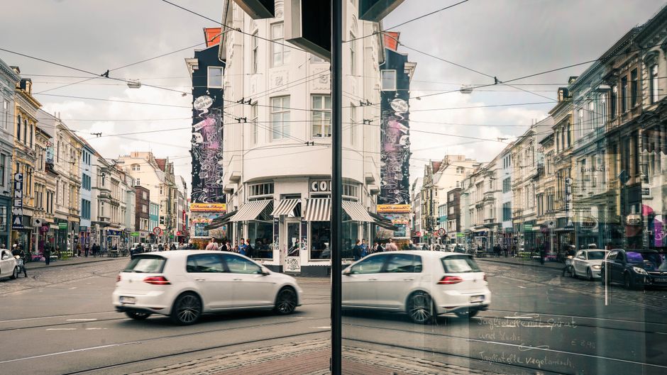 A bustling city street with dynamic reflections of cars and buildings on a glass facade.