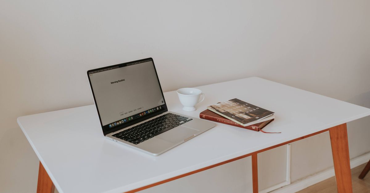 A person looking at a laptop with a coffee cup, thoughtful expression, minimalist desk setup