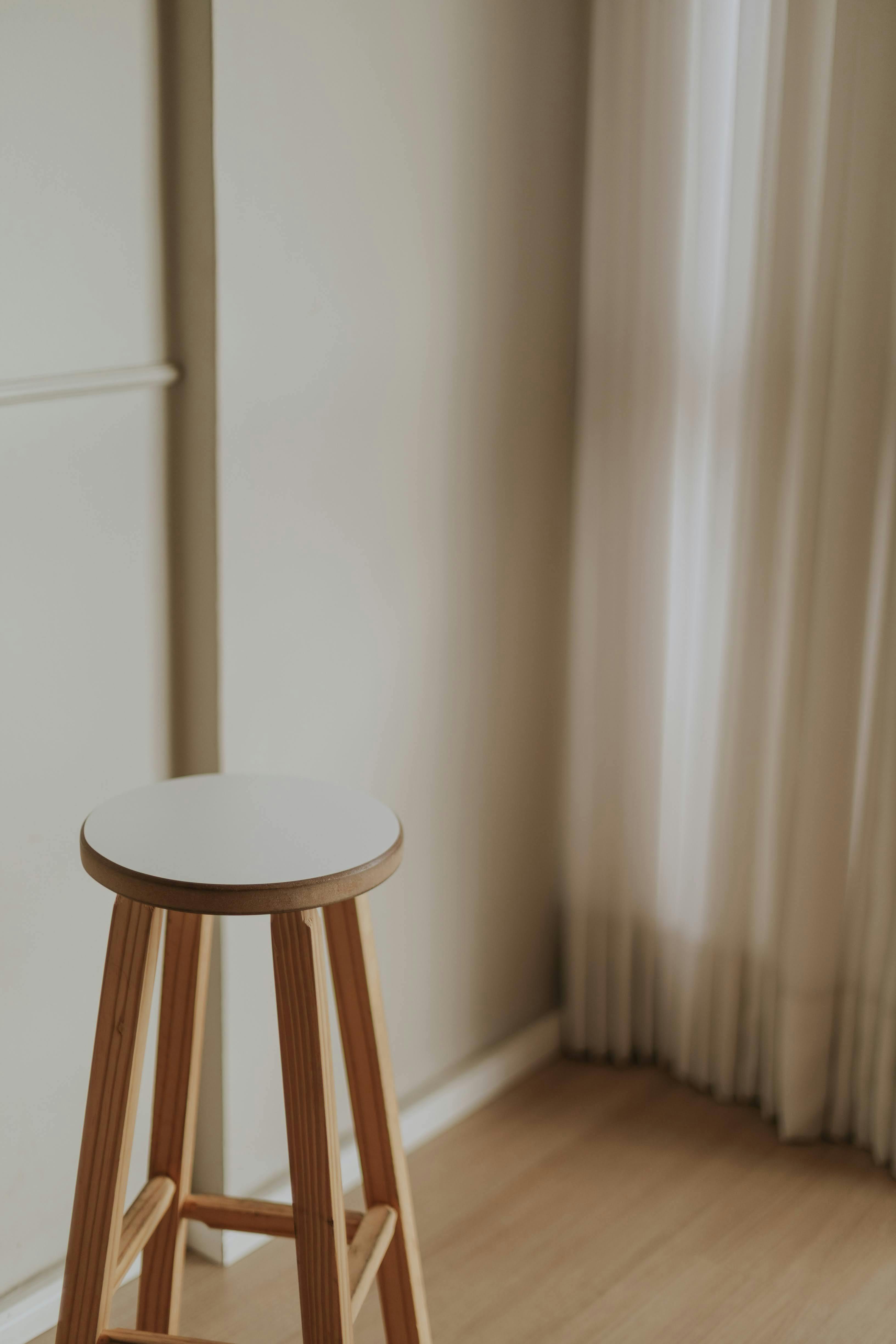 Bezpłatne Elegancki, minimalistyczny pokój z drewnianym stołkiem i delikatnym, naturalnym oświetleniem. Zdjęcie z galerii