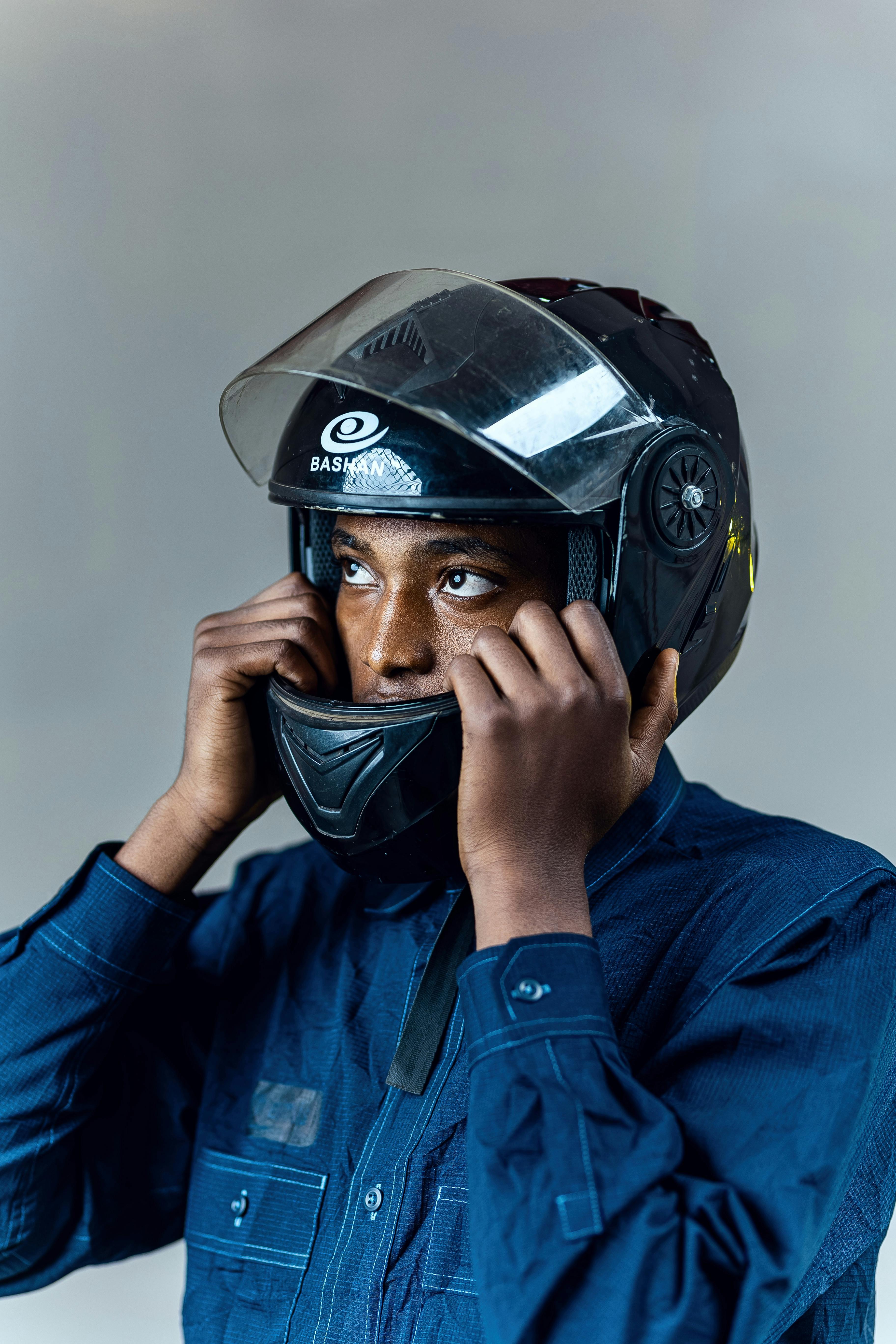 無料 青いシャツを着て、室内でバイクのヘルメットを調整している若い男性のポートレート。 写真素材