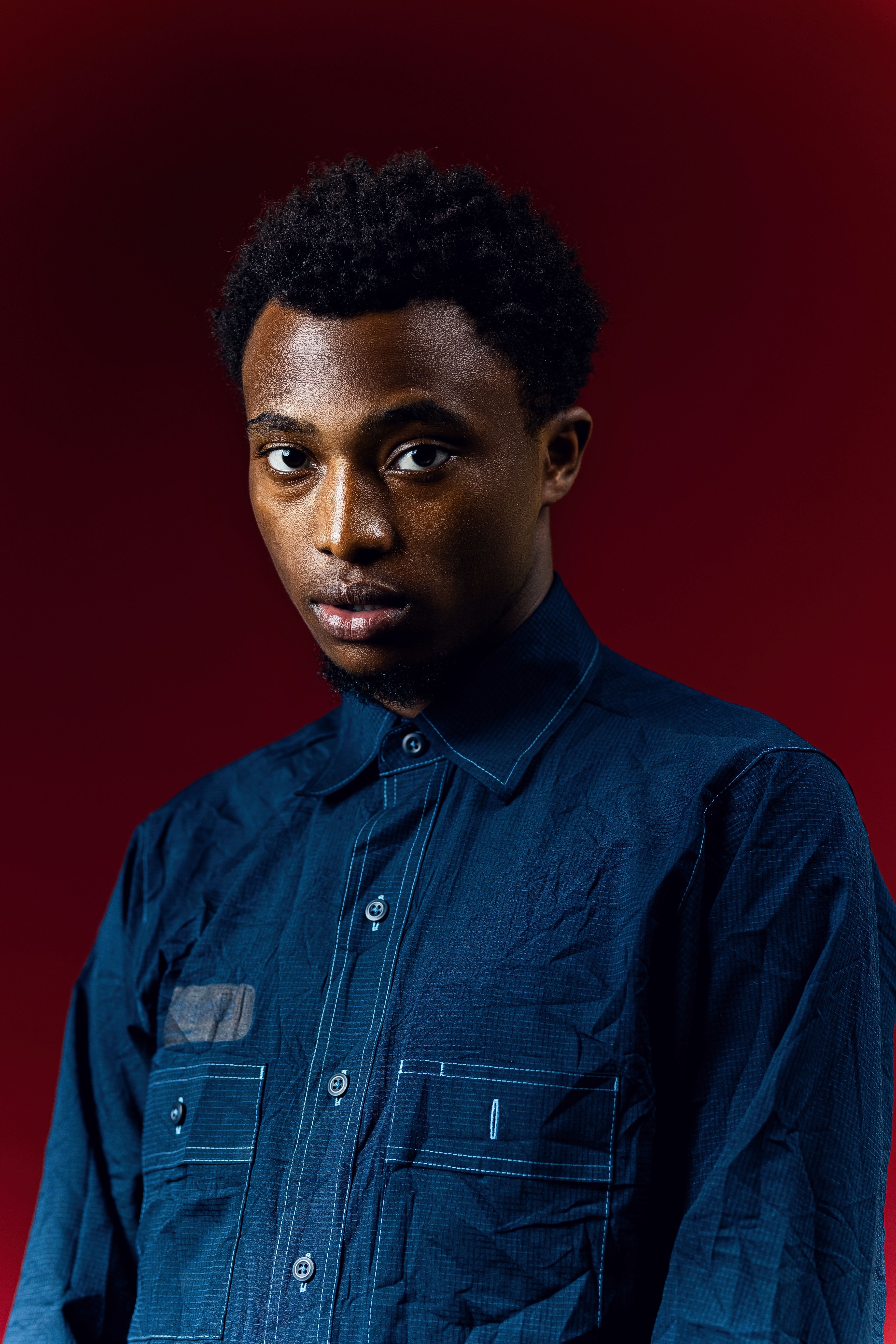 Confident man posing in a blue shirt against vibrant red backdrop.
