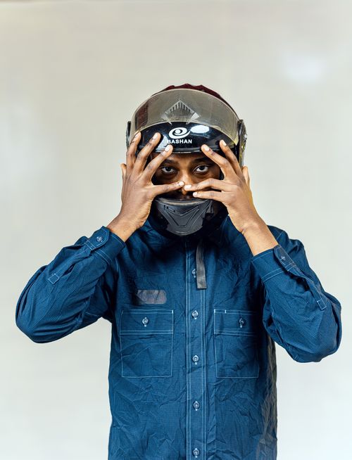 Free A man wearing a helmet and blue shirt peeks through his fingers with a neutral background. Stock Photo