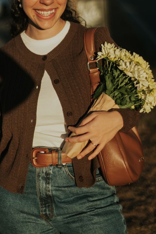 Free Smiling woman with white flowers, wearing casual attire outdoors in warm sunlight. Stock Photo