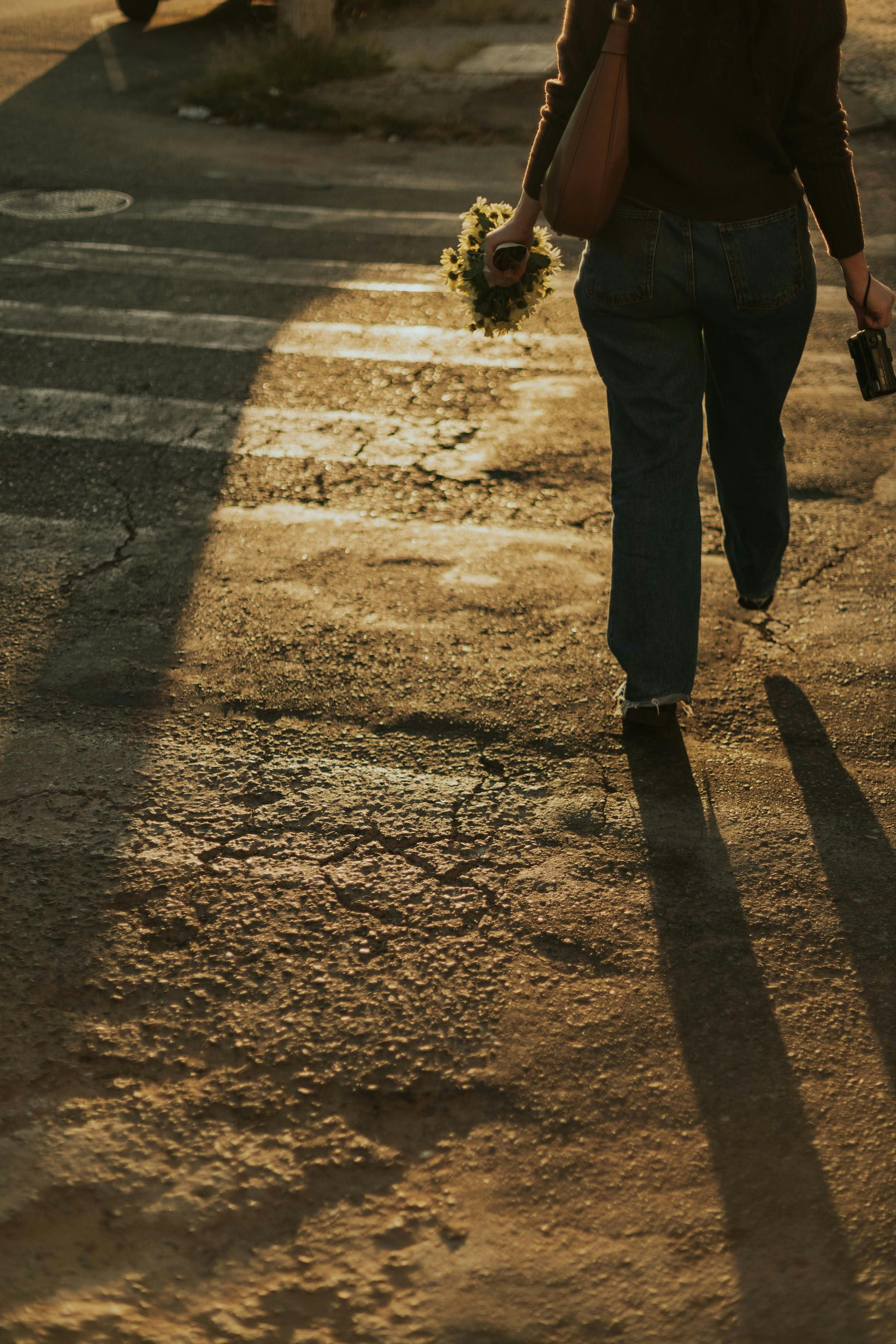 бесплатная Человек идёт по улице на закате, отбрасывая длинные тени, создавая расслабленную, тёплую атмосферу. Стоковое фото