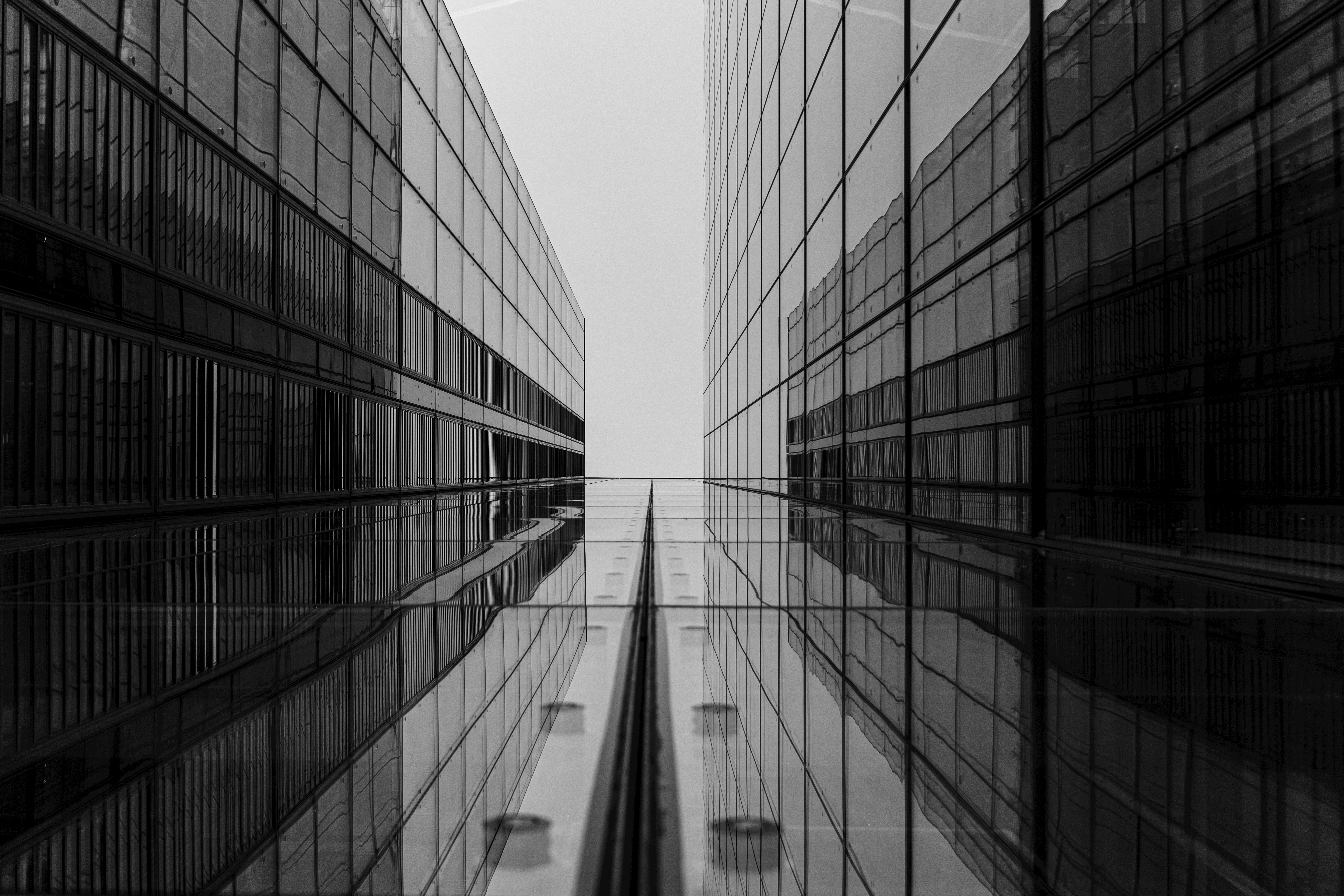 bezplatná Dramatický černobílý snímek zobrazující architekturu a odrazy moderní skleněné budovy. Základová fotografie