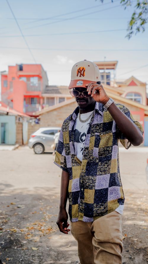 Free A fashionable man in sunglasses and cap poses confidently on a vibrant street in Nairobi, Kenya. Stock Photo