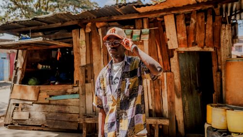 Free A fashionable young man stands confidently in front of a rustic wooden shop in Nairobi's vibrant streets. Stock Photo