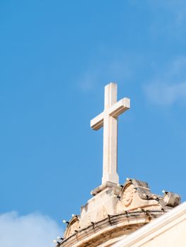 A serene image of a Christian cross atop a stone church roof under a clear blue sky.
