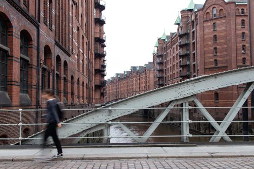 Free A person walks briskly on a bridge in Hamburg's iconic Speicherstadt district, showcasing historic brick architecture. Stock Photo