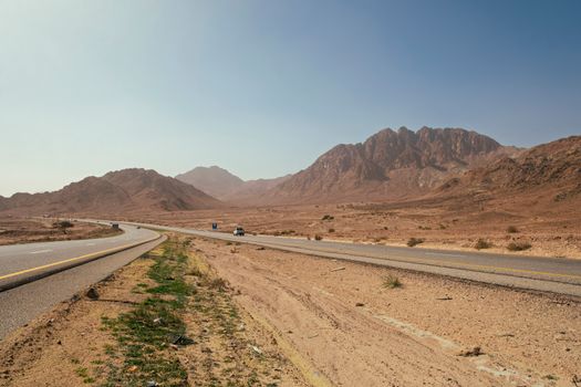 A winding road stretches through the desert landscape of Aqaba, Jordan, under a clear sky.