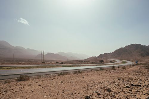 Free A scenic desert road curves through the mountainous landscape of Aqaba, Jordan, under a clear sky. Stock Photo