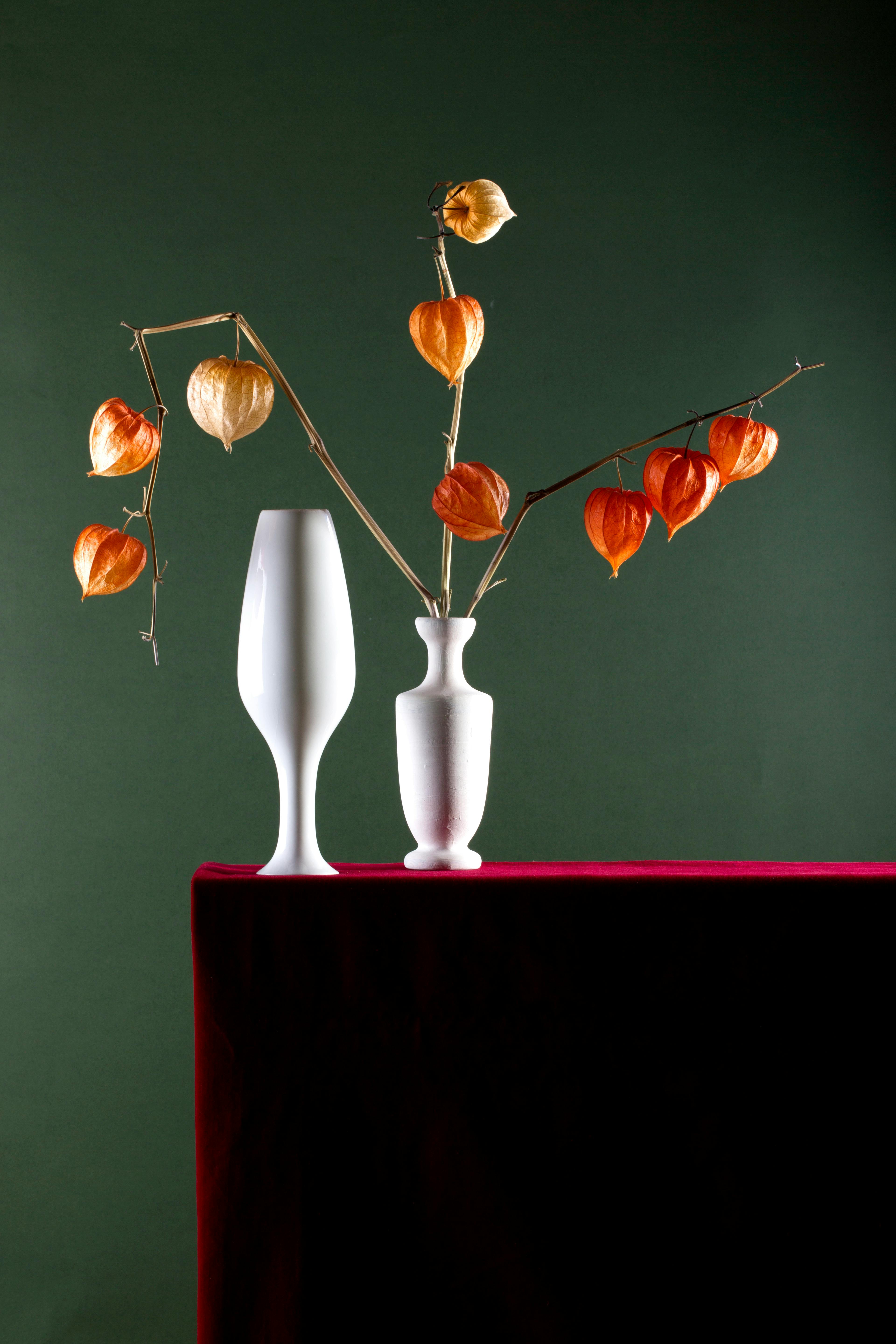 Miễn phí Một bức tranh tĩnh vật tối giản với những chiếc bình trắng cắm hoa physalis màu cam rực rỡ trên chiếc bàn nhung đỏ, trên nền xanh đậm. Ảnh lưu trữ