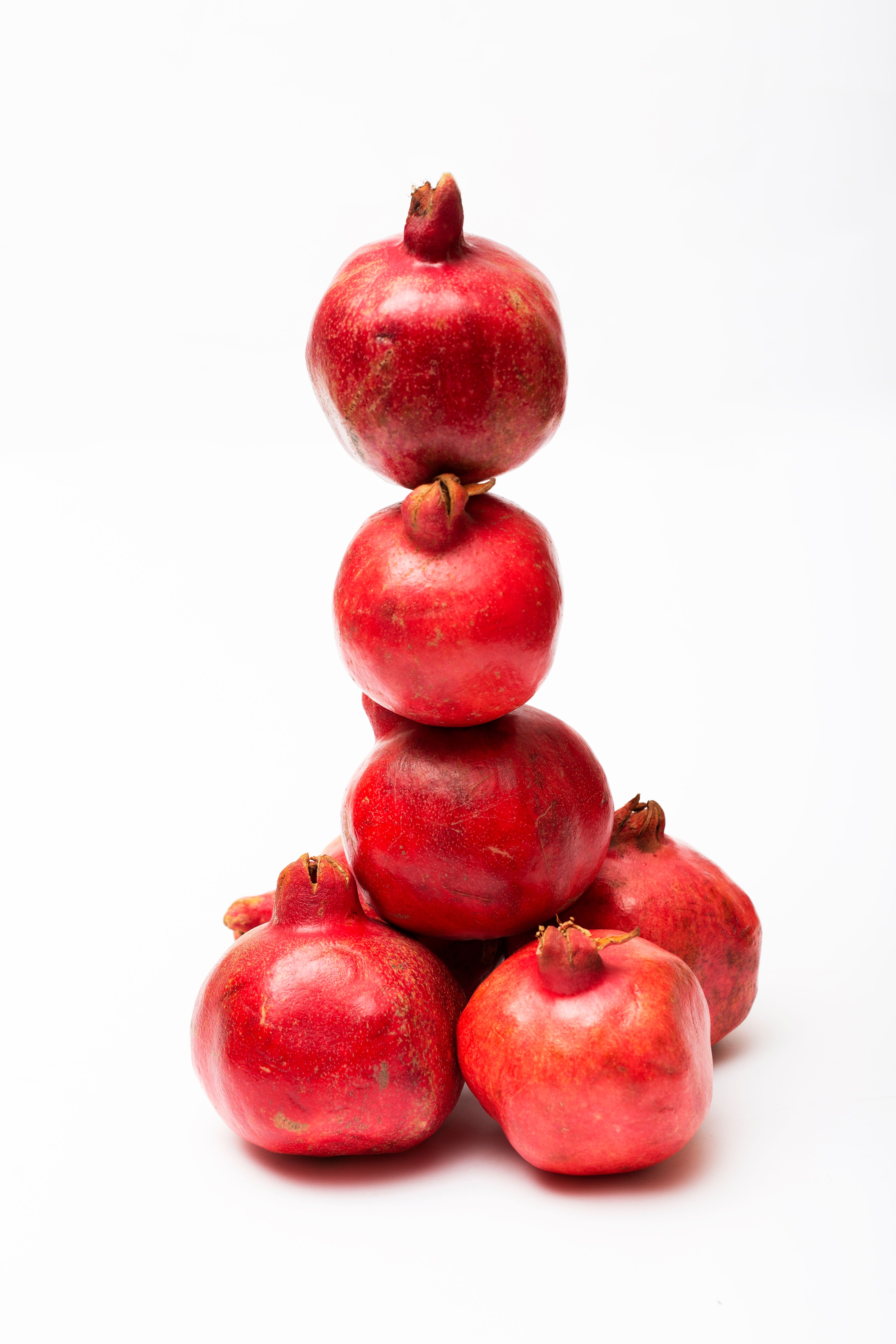 A creative stack of fresh red pomegranates on a white background, perfect for food and health themes.