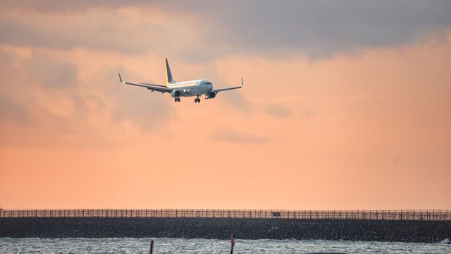 Airplane descending over ocean towards Bali Airport with sunset sky backdrop. — lounges at Bali Airport