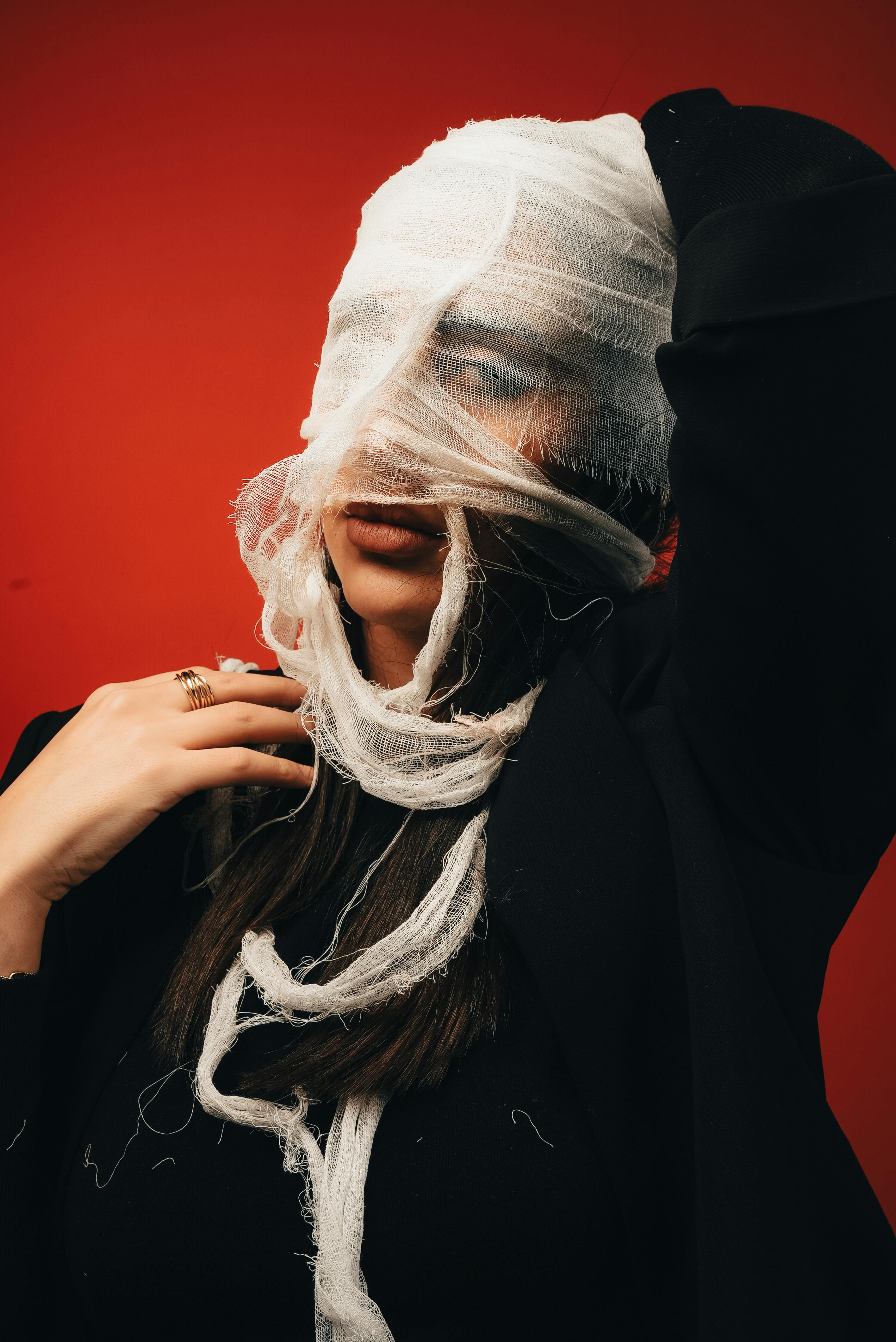 Free A creative portrait of a woman with face wrapped in fabric against a red background. Stock Photo