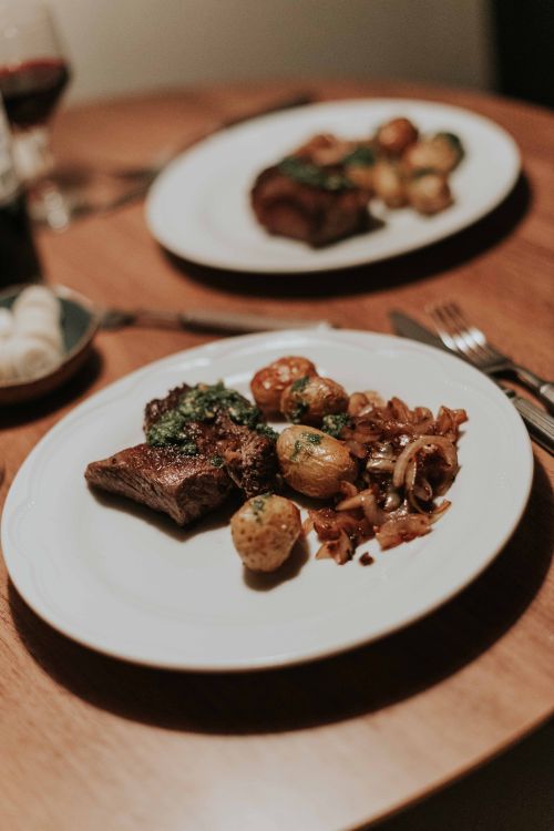 Free Tantalizing steak and herb potatoes on a beautifully set dinner table. Stock Photo