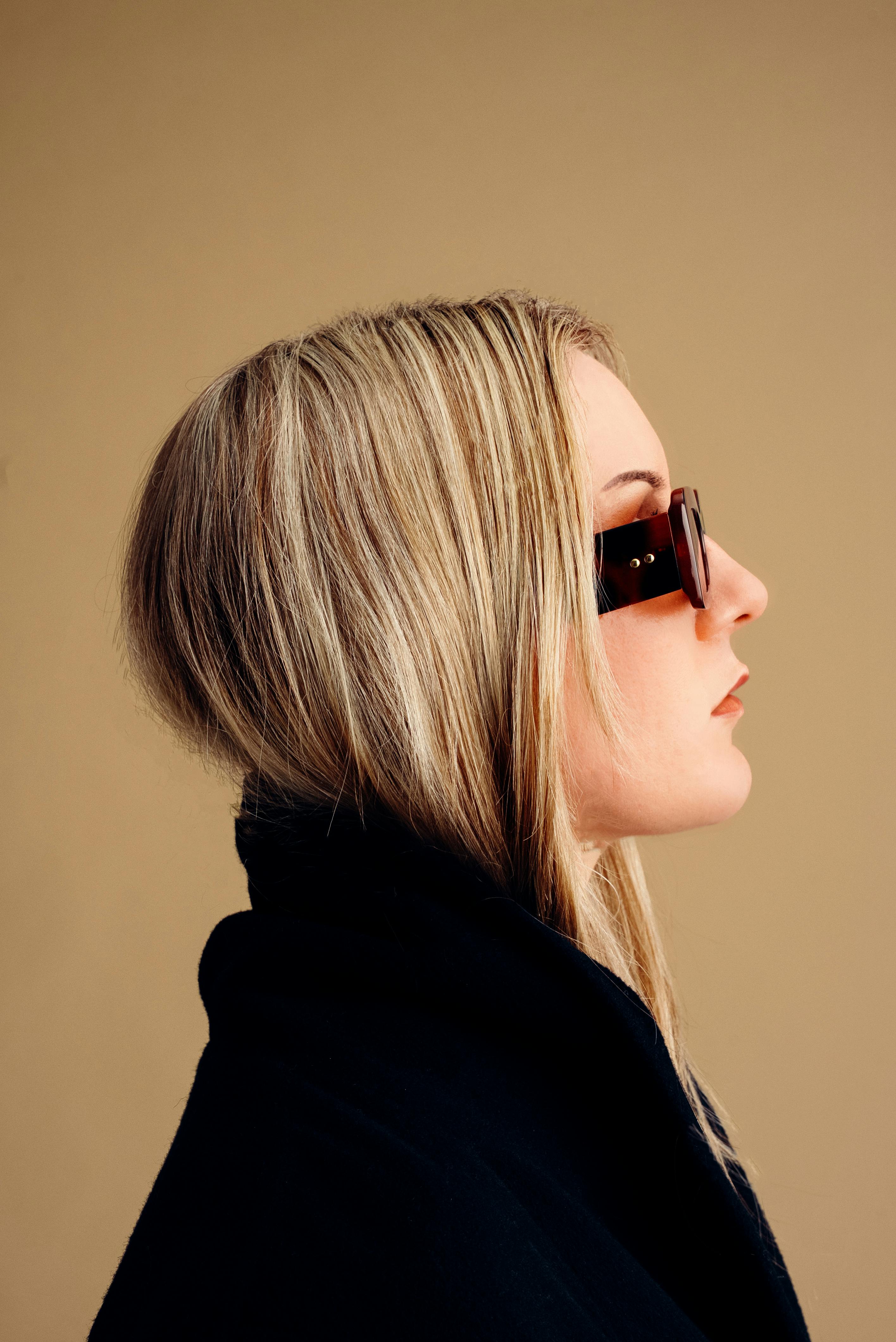 Side profile of a woman in sunglasses and a coat, exuding modern style.