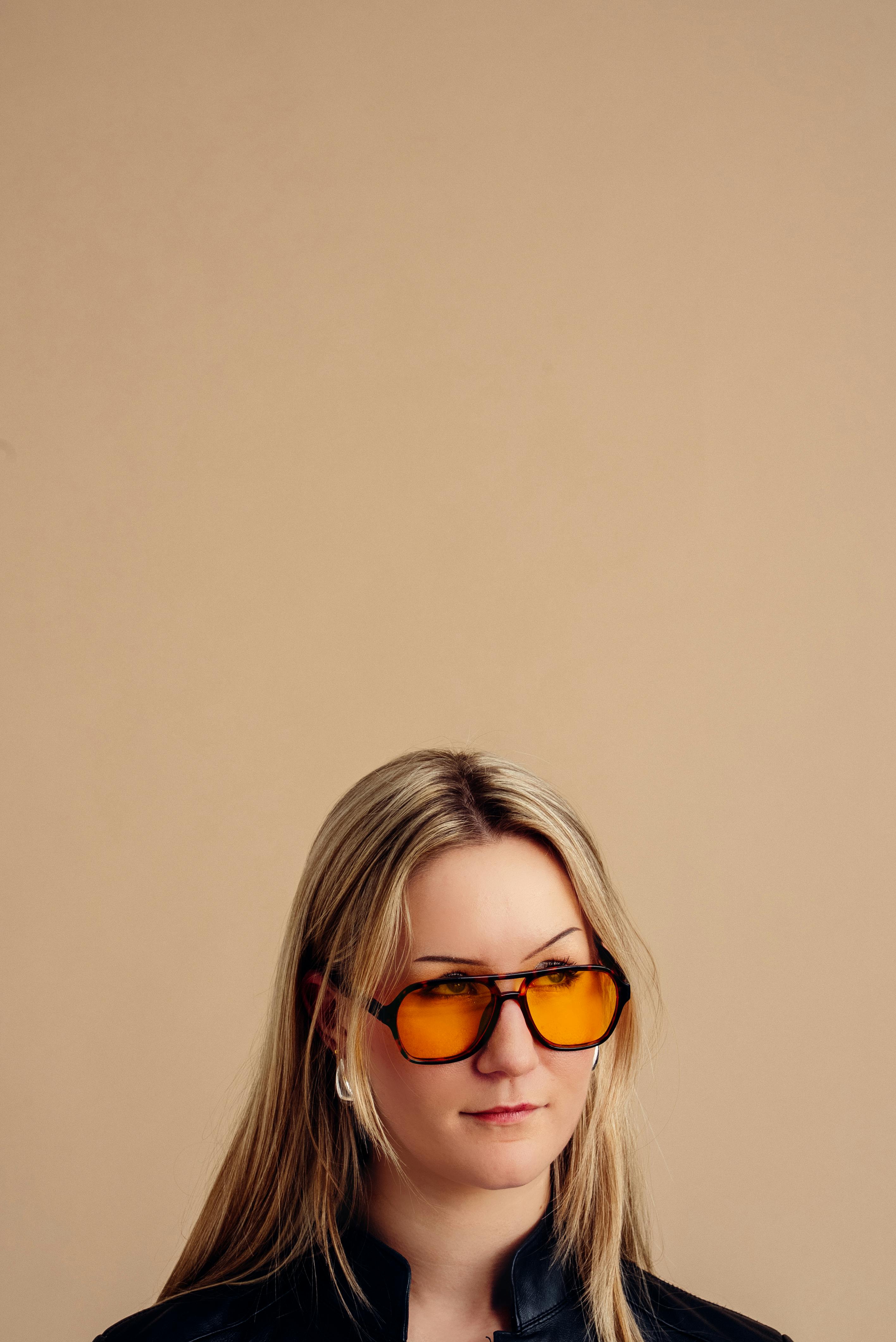 Gratis Donna alla moda che indossa occhiali da sole gialli e giacca nera su sfondo neutro. Foto a disposizione