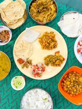 A vibrant Indian thali platter with chickpeas, chutneys, and roti on a colorful tablecloth.