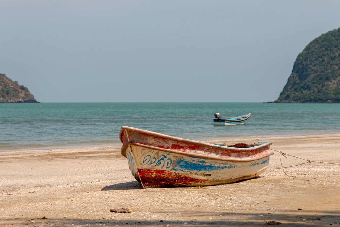 A small weathered Thai fishing boat resting on an empty sandy beach