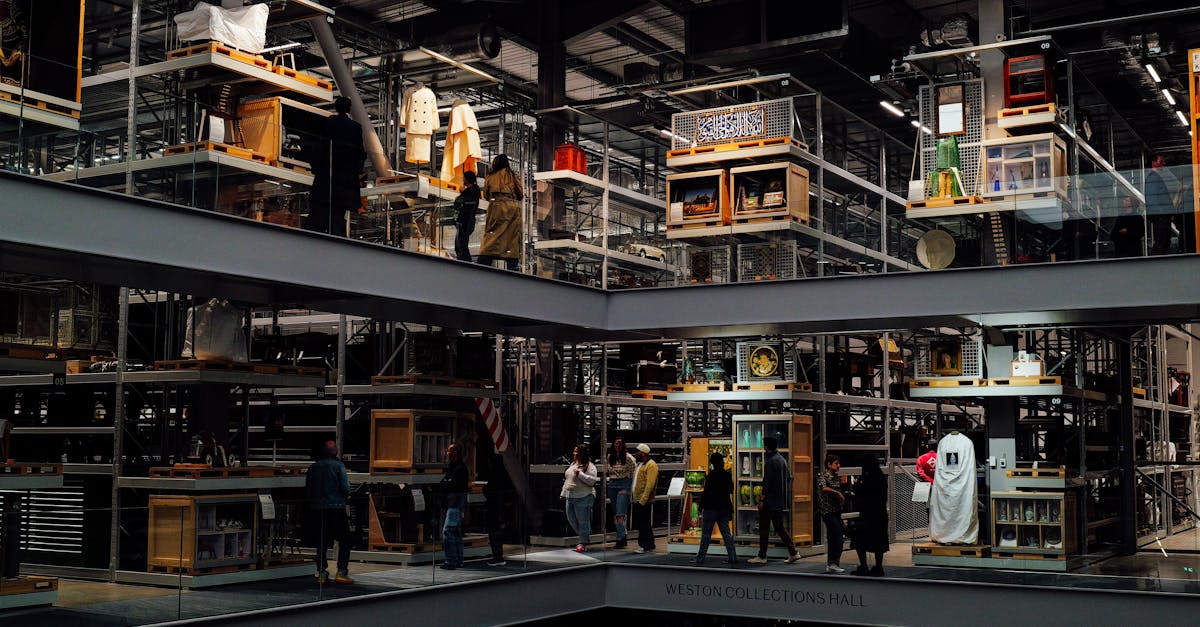 Photo by Adrien Olichon A multilevel industrial warehouse interior with people observing exhibits on each floor.