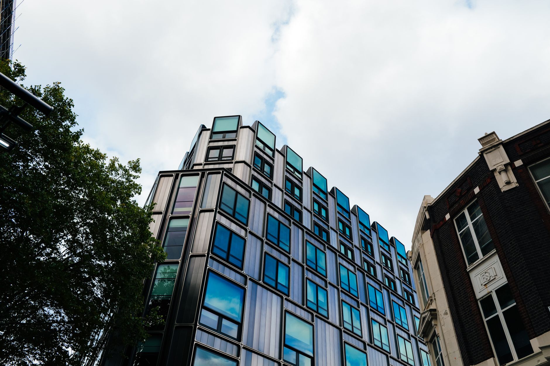 A contemporary building with reflective windows in an urban setting under a cloudy sky.