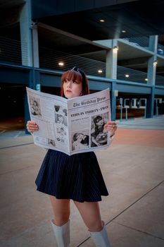 Stylish woman reads a newspaper with creative birthday theme outdoors, showcasing modern fashion.