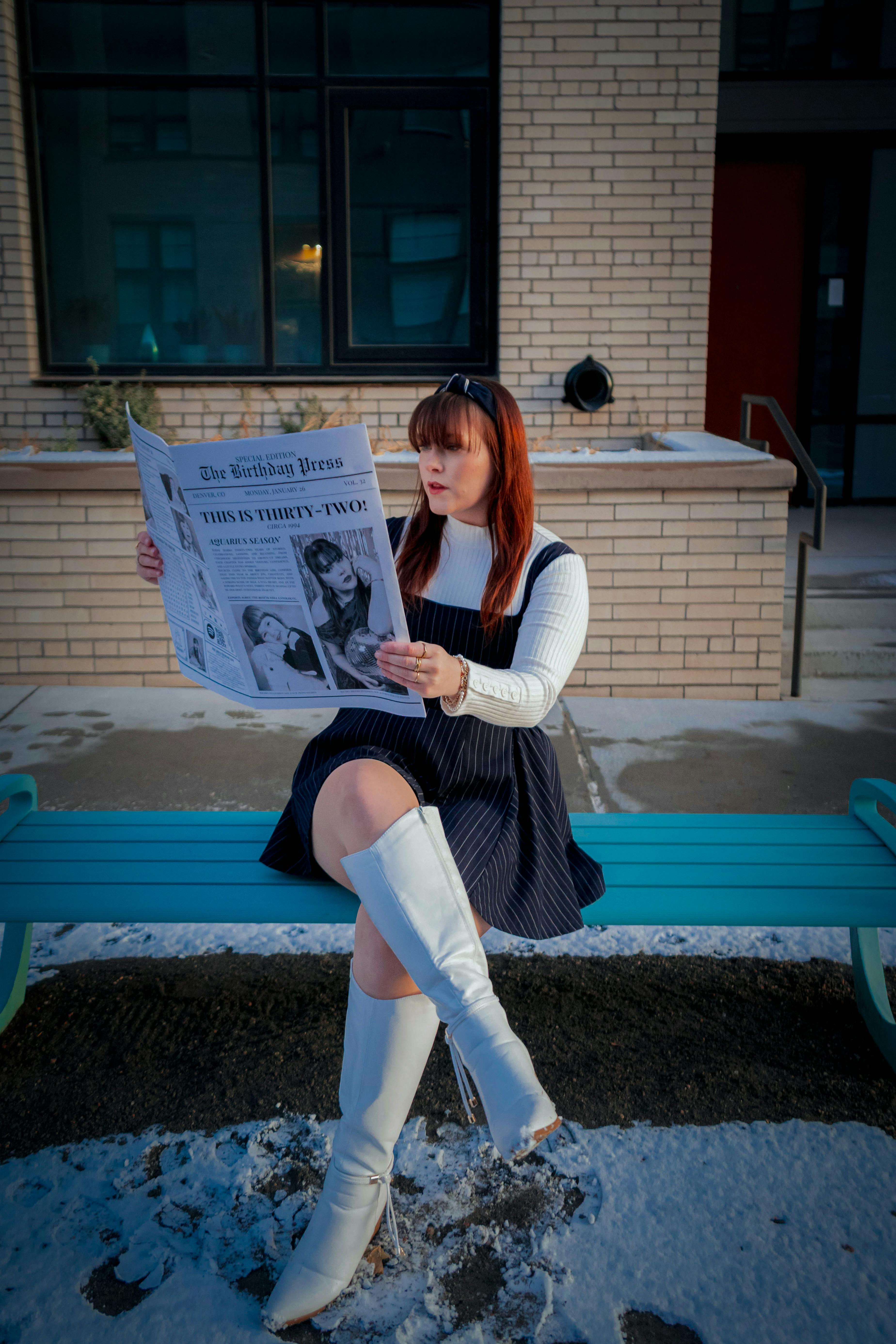 gratis Een vrouw in winterkleding leest de krant op een besneeuwde bank, waarbij ze een moderne stijl combineert met een klassieke stedelijke sfeer. Stockfoto