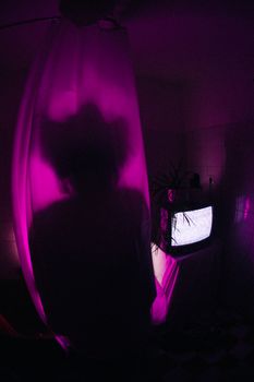 Eerie silhouette behind curtain with neon lighting and glowing TV, evoking mystery. — photo by Dark Indigo