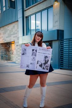 Fashionable woman in urban setting posing with a unique newspaper prop. City vibes with editorial flair.