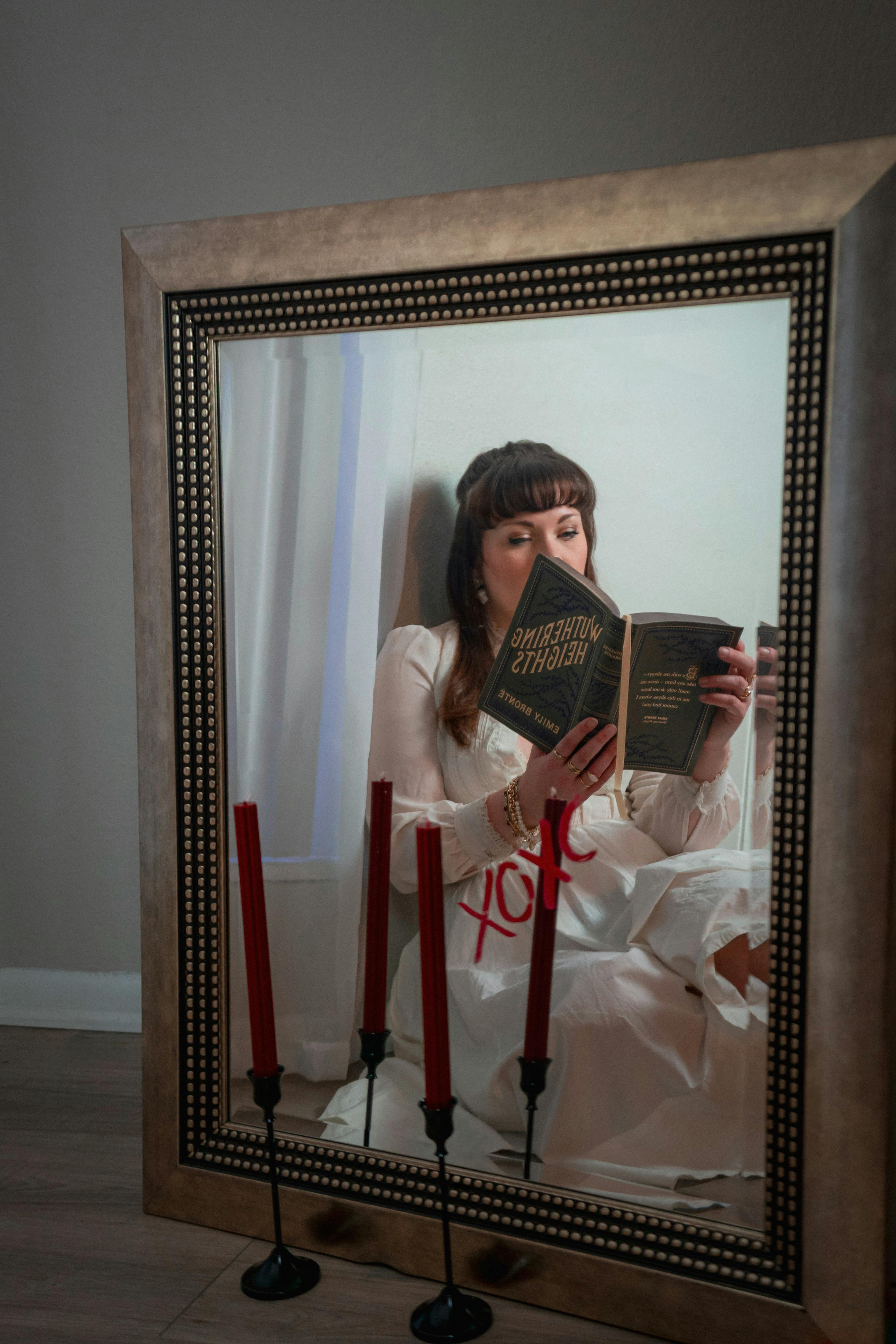 Ücretsiz Bir kadın, antika dekorasyon ve kırmızı mumlarla çevrili bir ortamda, aynadaki yansımasında kitap okuyor. Stok Fotoğraflar