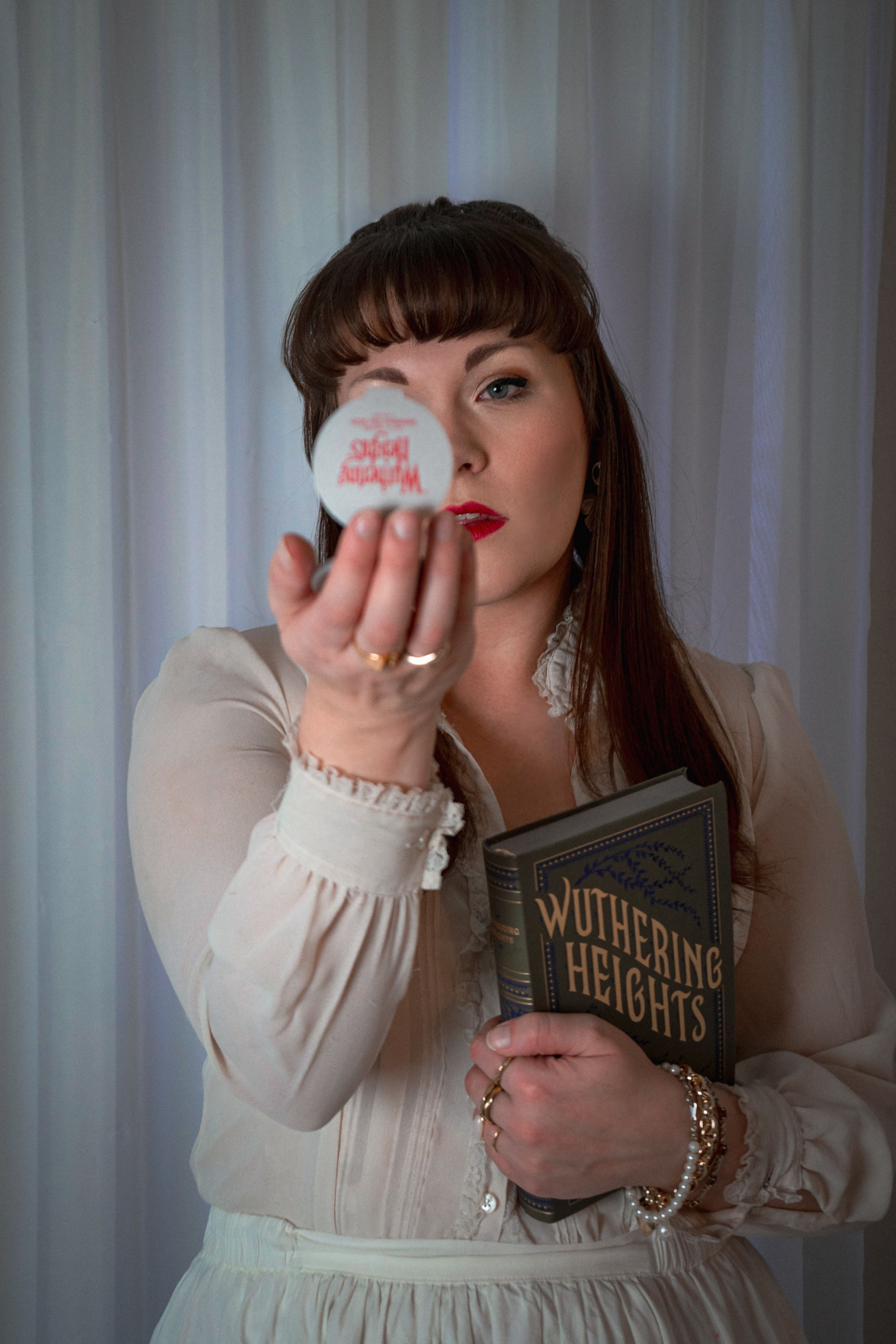 Elegant portrait of woman holding 'Wuthering Heights' with vintage aesthetic and reflective object.