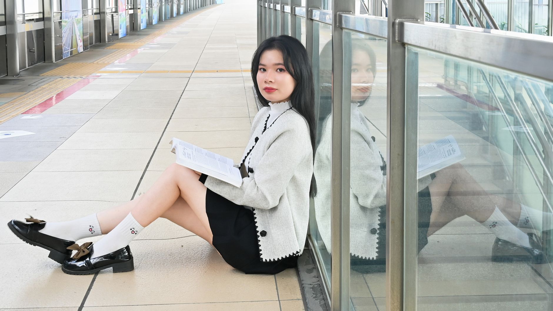 Elegant young woman reading a book in a quiet indoor urban setting.