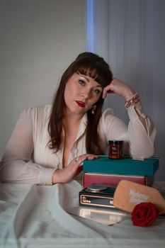 A creative portrait of a woman in vintage style surrounded by books and a rose indoors.