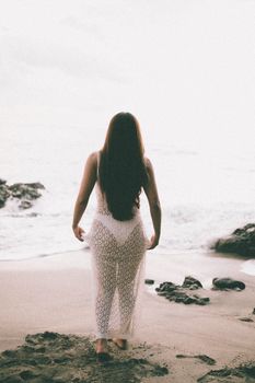 A woman in a white dress walks along a quiet beach, embracing the tranquil evening atmosphere.