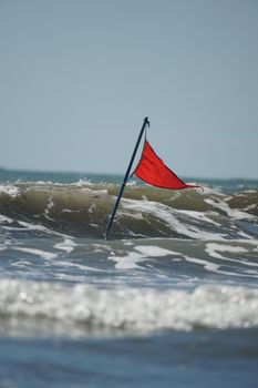 A red warning flag flying on a sandy beach during a high surf warning