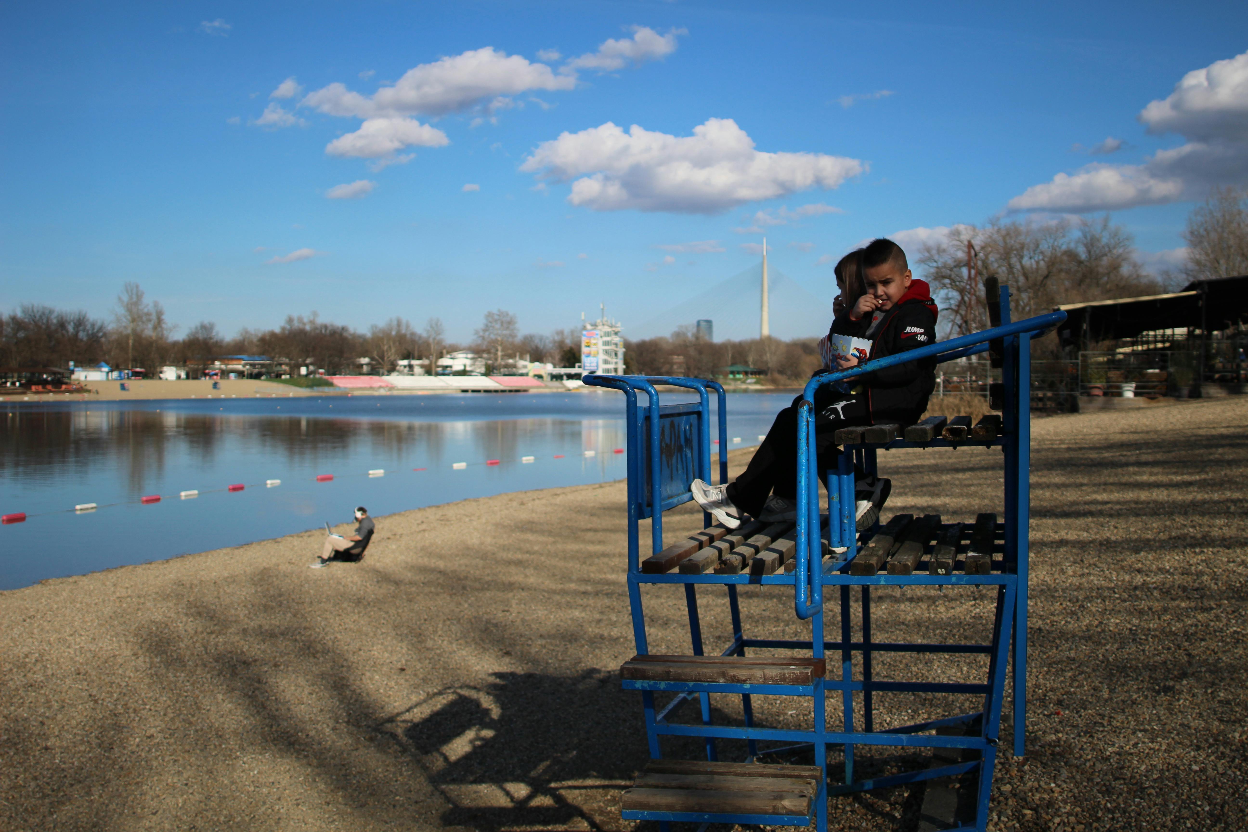 無料 晴れた日に静かな川のビーチを見渡しながらライフガードの椅子に座っている子供。 写真素材
