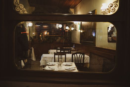 Warm and inviting vintage restaurant interior seen through a window at night with elegant table settings.