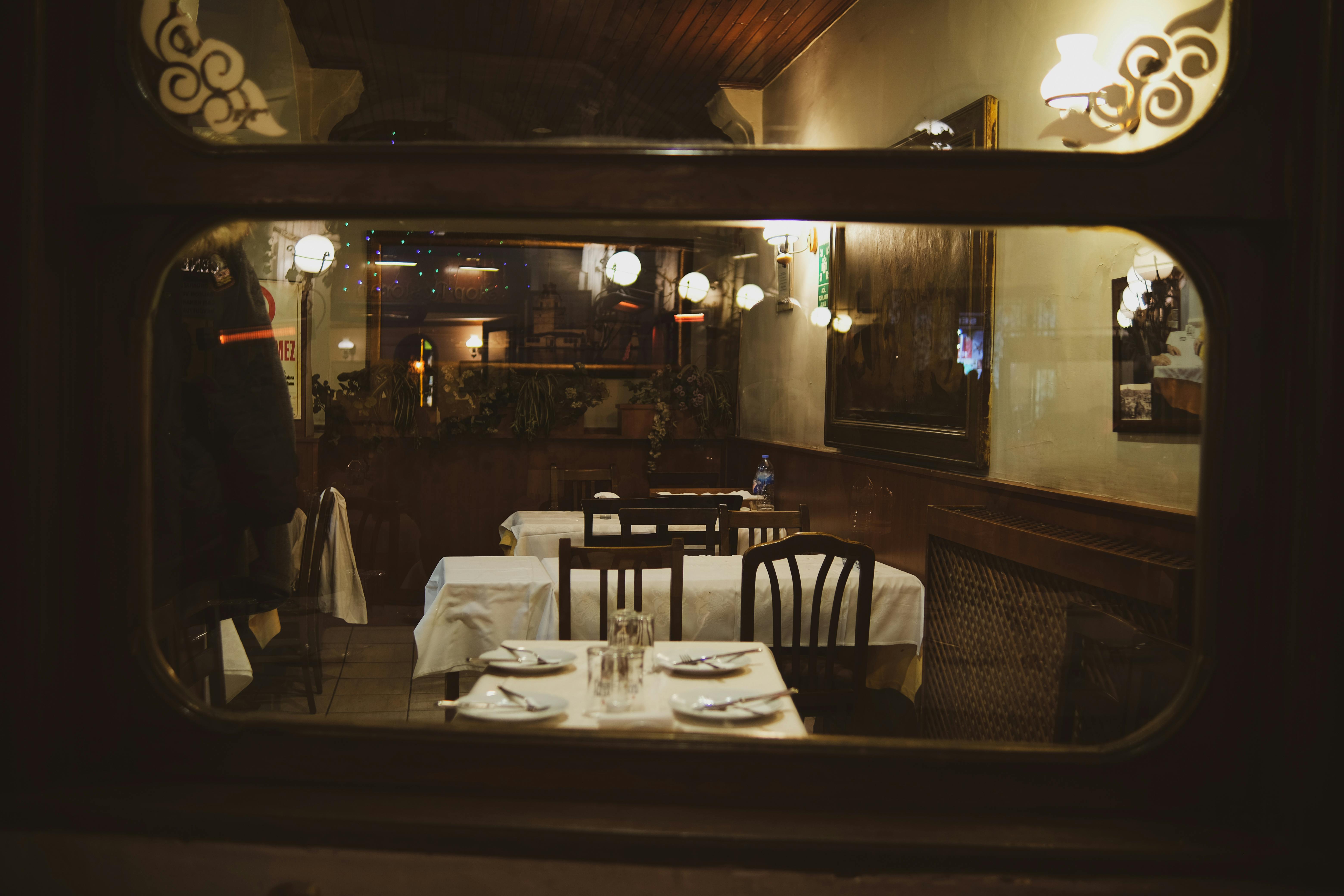 Gratis Interior restoran vintage yang hangat dan mengundang, terlihat dari jendela di malam hari dengan penataan meja yang elegan. Foto Stok