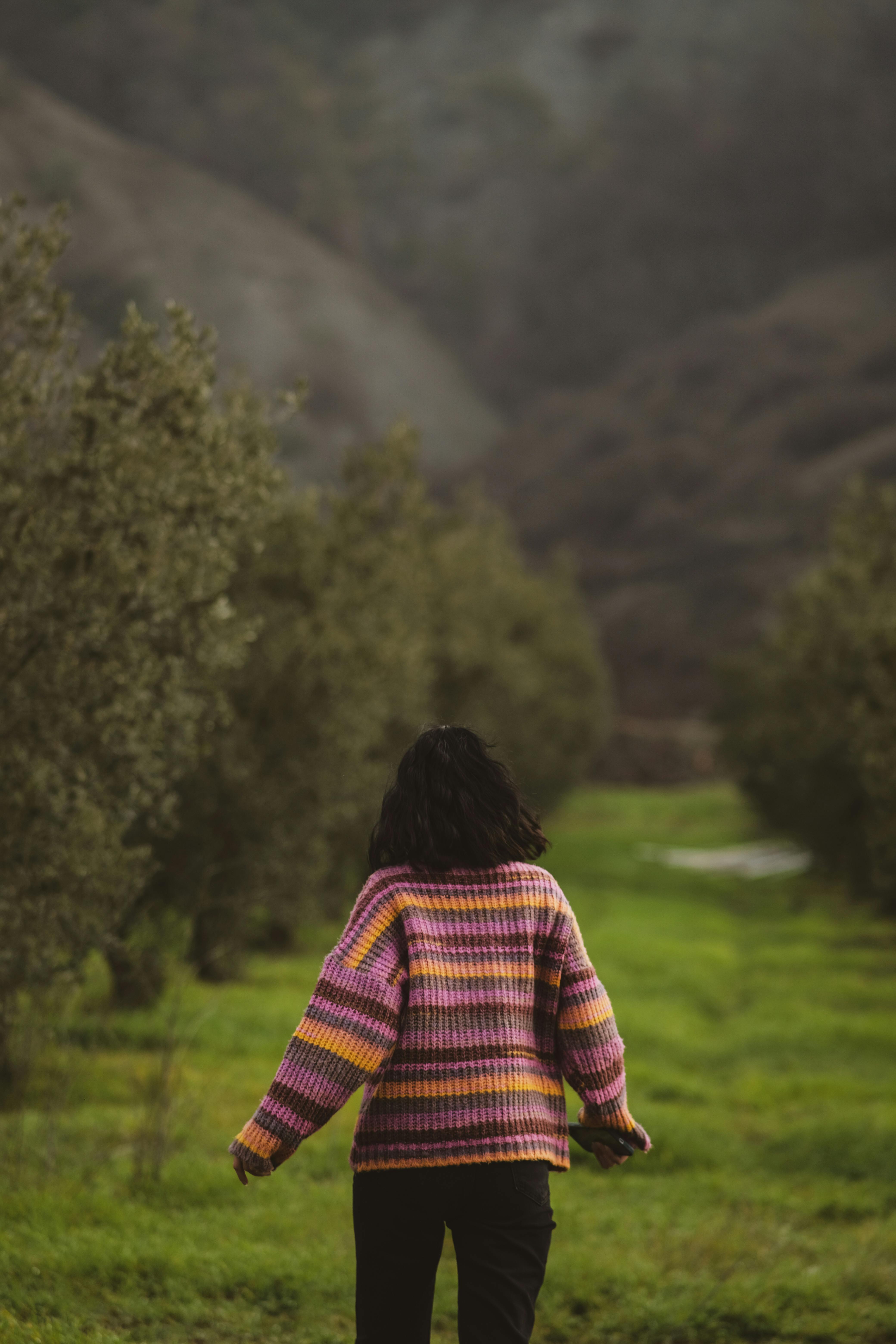 ฟรี ชายคนหนึ่งสวมเสื้อกันหนาวสีสันสดใสกำลังเดินผ่านทางเดินสีเขียวที่รายล้อมไปด้วยธรรมชาติ คลังภาพถ่าย