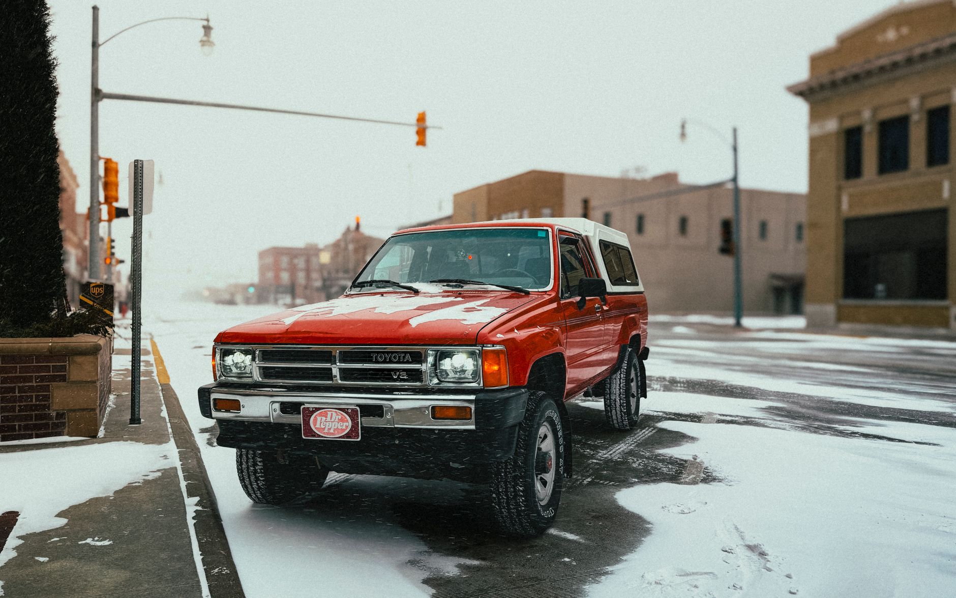 Red vintage Toyota truck parked in a snowy urban street with classic architecture.